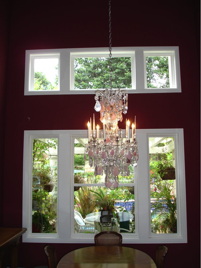 A chandelier hanging from the ceiling in front of two windows.