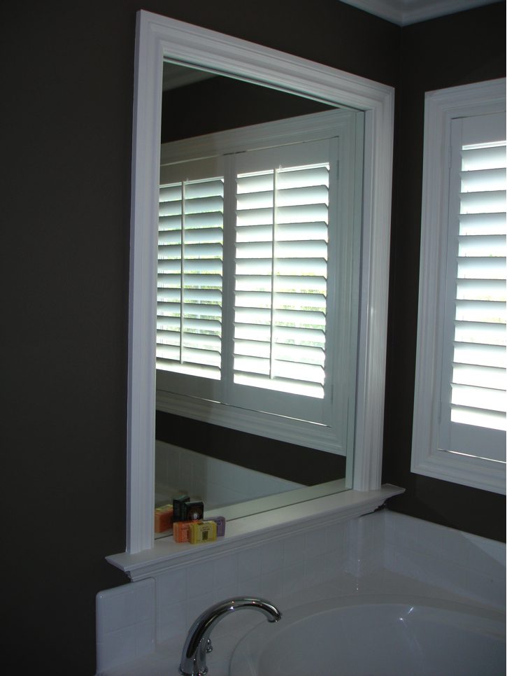 A bathroom with a large mirror and white shutters.