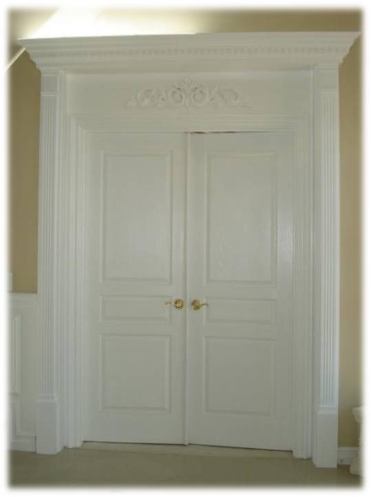 A white door with two brass knobs and a crown molding.