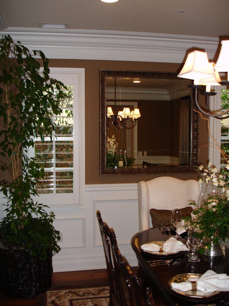 A dining room with a table and chairs, a mirror and plants.